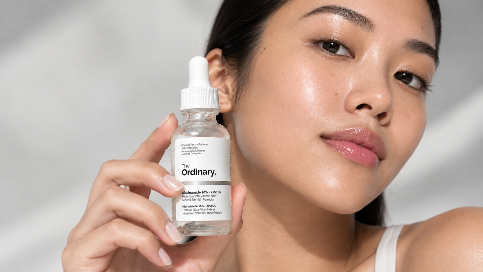 Woman holding The Ordinary Niacinamide 10% + Zinc 1% serum beside her face